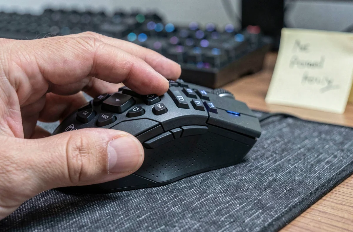 Gros plan sur les boutons programmables d'une souris MMO tenue en main sur un tapis de souris
